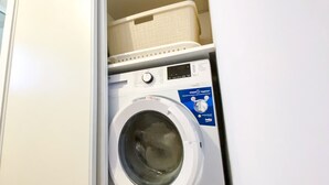 Eine Waschmaschine mit Frontlader in einem Waschraum, darüber ein Wäschekorb.