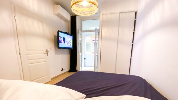 Ein Schlafzimmer mit einem Bett, einem an der Wand montierten Fernseher und einer Tür, die auf einen Balkon führt.