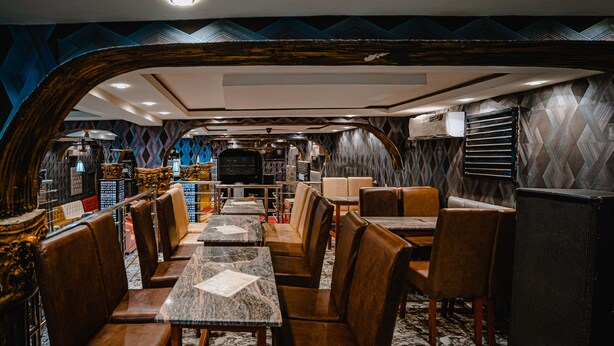 Een restaurant met marmeren tafels en lederen zitjes, met een patroonwand en een grote spiegel.