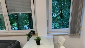 Een moderne eetruimte met een marmeren tafel, witte stoelen met bekleding en een potplant.