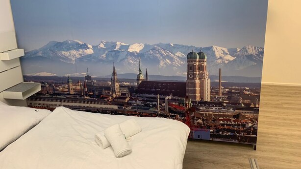 Een slaapkamer met een bed, een wit kussen en een keurig opgevouwen witte handdoek.