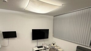 Een moderne woonkamer met een grijze bank, twee flatscreentelevisies aan de wand, een witte tv-kast en een kleine ronde tafel met een plant.