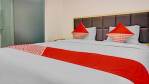 Un lit avec une couvre-lit blanche et rouge, deux oreillers rouges avec un motif blanc, et une tête de lit grise.