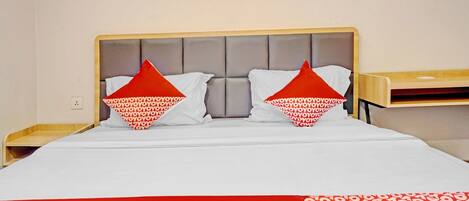 A hotel room with a bed, two pillows, a red and white patterned blanket, and a wooden nightstand.
