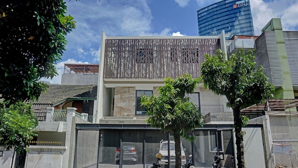 Un bâtiment moderne doté d’une grande façade en verre, d’une clôture métallique et de deux arbres au premier plan.