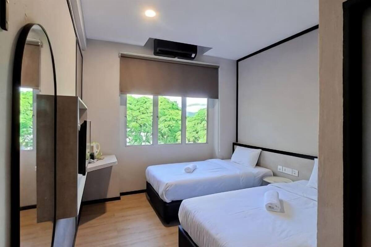 Une chambre d’hôtel avec deux lits, un bureau, un miroir et une fenêtre donnant sur un paysage verdoyant.