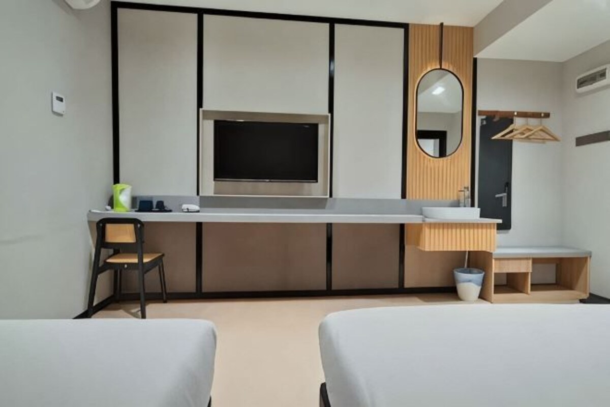 A hotel room with a bed, a desk with a TV, a mirror, and a small seating area.