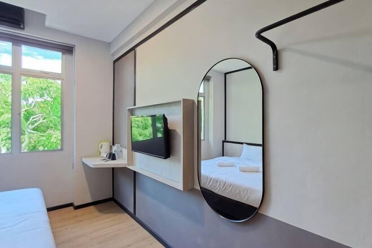 Une chambre à coucher comprenant un lit, un téléviseur fixé au mur, une table de chevet, un miroir et une fenêtre donnant sur un paysage verdoyant.