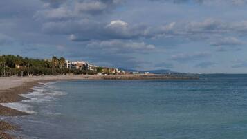 A coastal beach scene with a building on the shore, a rocky shoreline, and a clear sky.