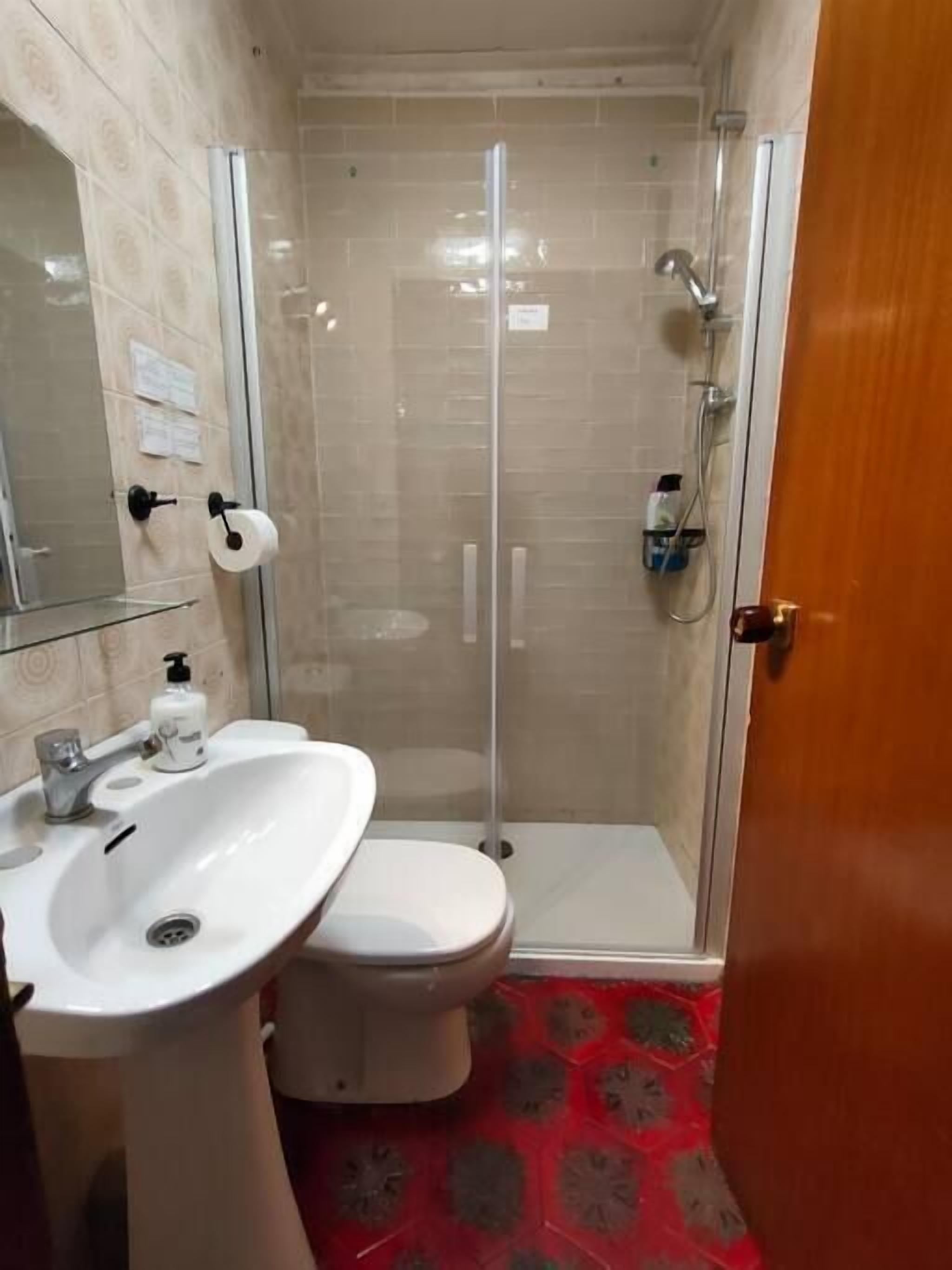 Un baño con inodoro, lavamanos y ducha con mampara de vidrio.