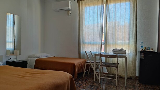 A hotel room with two beds, a desk with a chair, a mirror, an air conditioner, and a window with curtains. - Pensión Benavente. 5 - (Playa 1,5km / AP7-3min) (Moncofa)