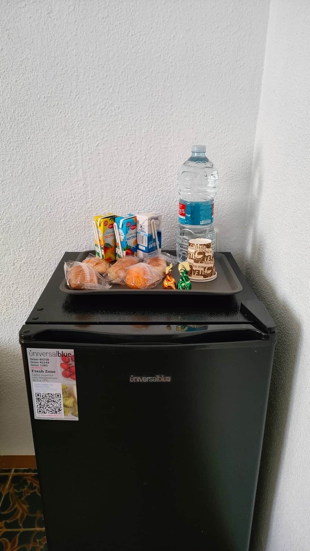 Un réfrigérateur noir rempli de produits alimentaires et une bouteille d’eau.