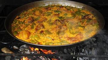 Een grote pan met een rijstgerecht, mogelijk paella, kookt op een open vuur.