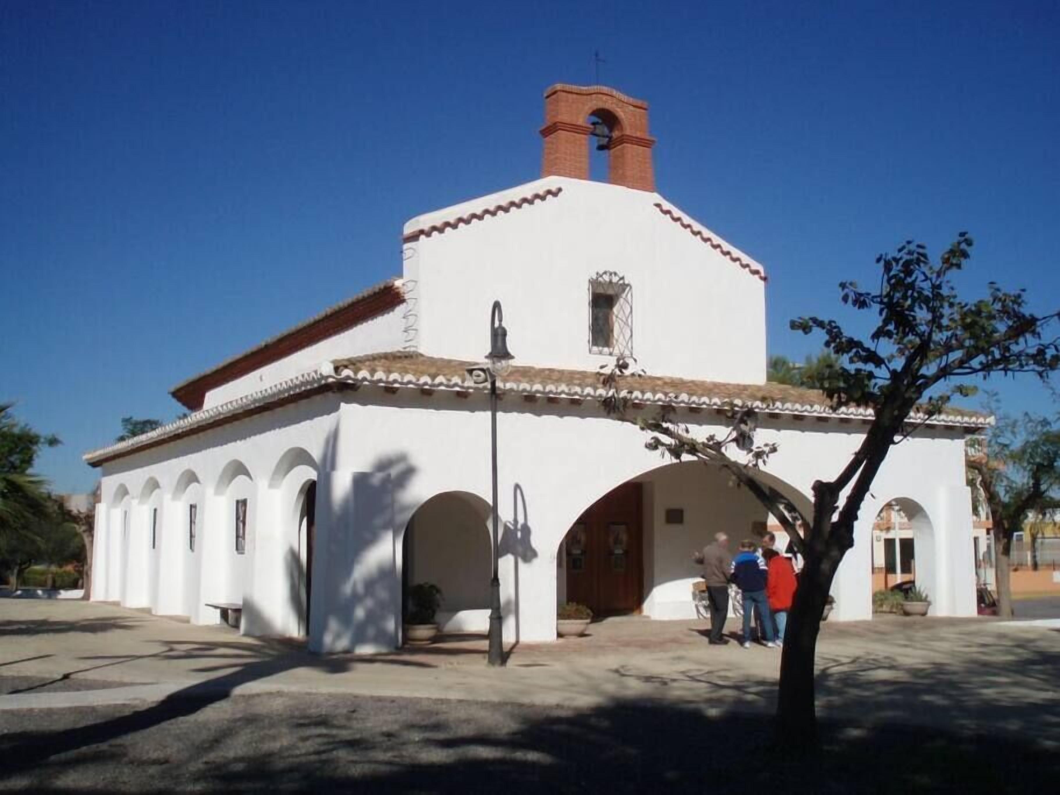 Un edificio blanco con techo de tejas rojas, una torre de campana y arcos.