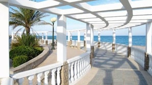A covered walkway with white railings, palm trees, and a view of the sea. - Paradis I (with seaviews) (El Grau de Moncofa)