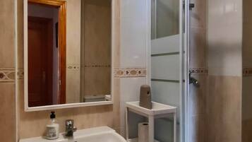 Un baño con lavabo blanco, espejo y cabina de ducha de vidrio.