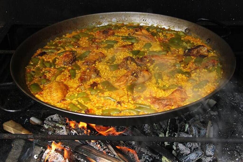 Una paellera grande llena de un plato de arroz, posiblemente paella, cocinándose sobre fuego abierto.