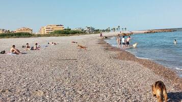 Una playa de guijarros con gente tomando el sol y caminando por la orilla.
