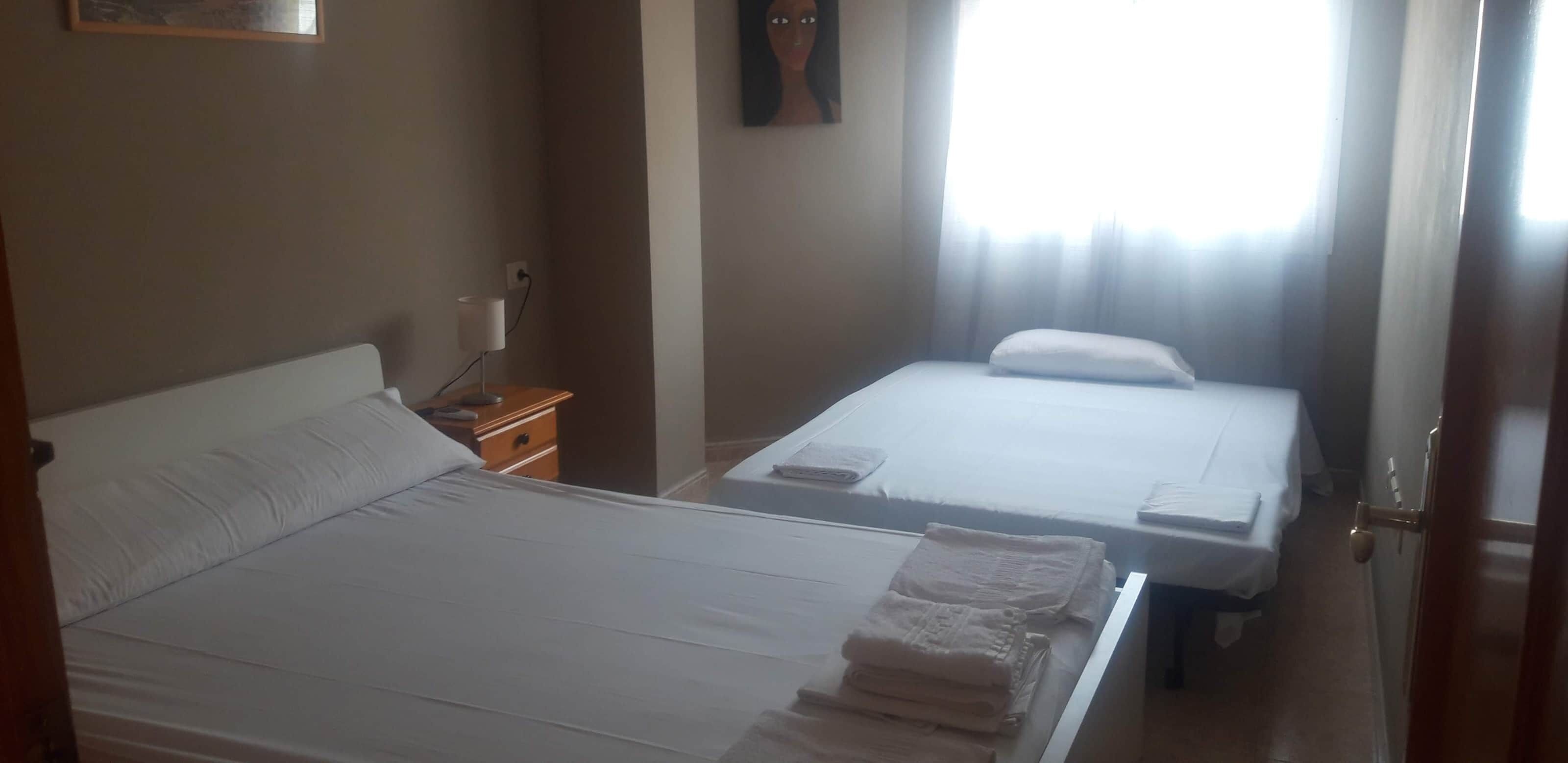 Une chambre d’hôtel avec deux lits, une table de chevet, une lampe et une fenêtre avec des rideaux.