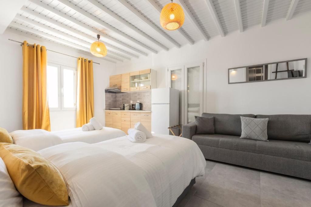 Habitación de hotel con dos camas, un sofá, zona de cocina y un ventanal con cortinas.