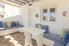 A room with a white table, a bench with blue cushions, a window with a view, and a door. - Mykonos Eight (Mykonos)