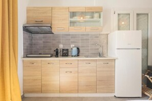 A modern kitchen with wooden cabinets, a built-in oven, a coffee maker, and a refrigerator. - Mykonos Eight (Mykonos)