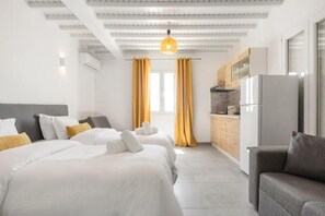 A hotel room with two beds, a sofa, a kitchen area, and a large window. - Mykonos Eight (Mykonos)