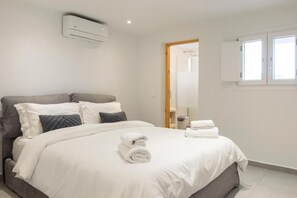 A hotel room with a bed, a mirror, a window, and an air conditioning unit. - Mykonos Eight (Mykonos)