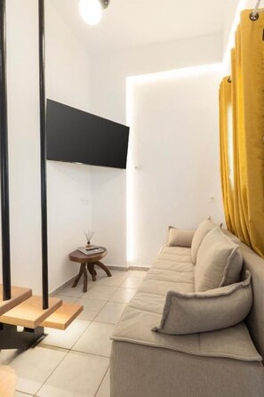 A modern living room with a sofa, a small side table, and a wall-mounted TV. - Mykonos Eight (Mykonos)