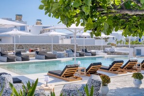 A poolside area with lounge chairs and umbrellas, surrounded by white buildings with stone walls. - Mykonos Eight (Mykonos)