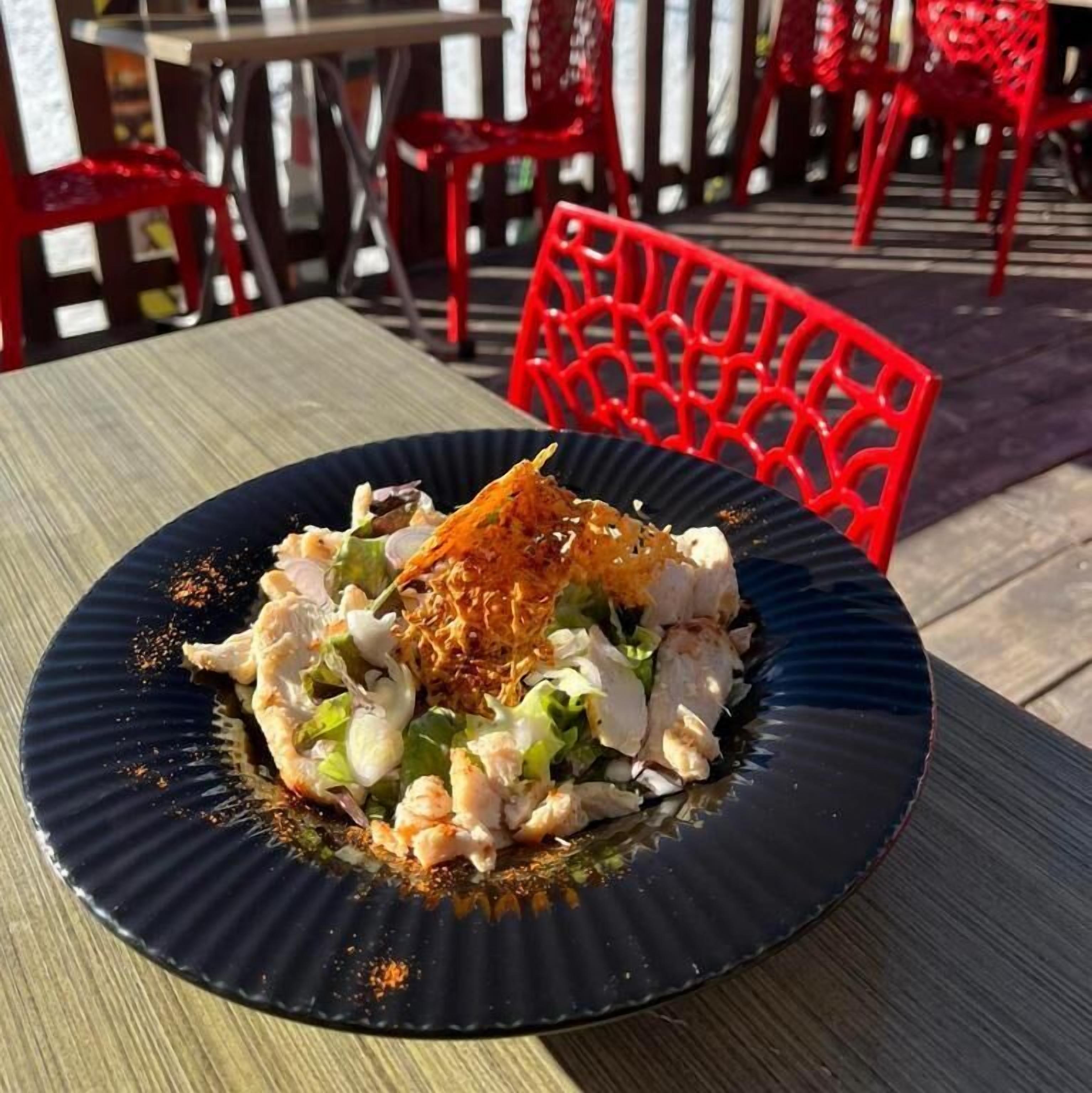 A plate of food on a table with red chairs in the background.