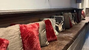 A seating area with a wooden bench, red and beige cushions, and a mounted ski. - Chalet Sainte Anne (La Condamine-Chatelard)
