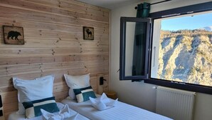A room with two beds, wooden panel walls, a window with a mountain view, and a mirror. - Chalet Sainte Anne (La Condamine-Chatelard)