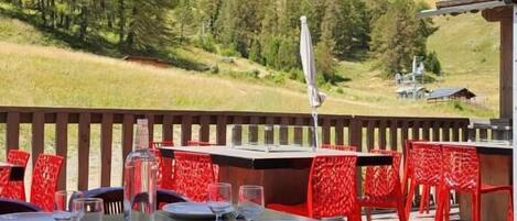 Un espace extérieur aménagé pour les repas, avec des tables et des chaises, une terrasse en bois et une chaîne de montagnes en arrière-plan.