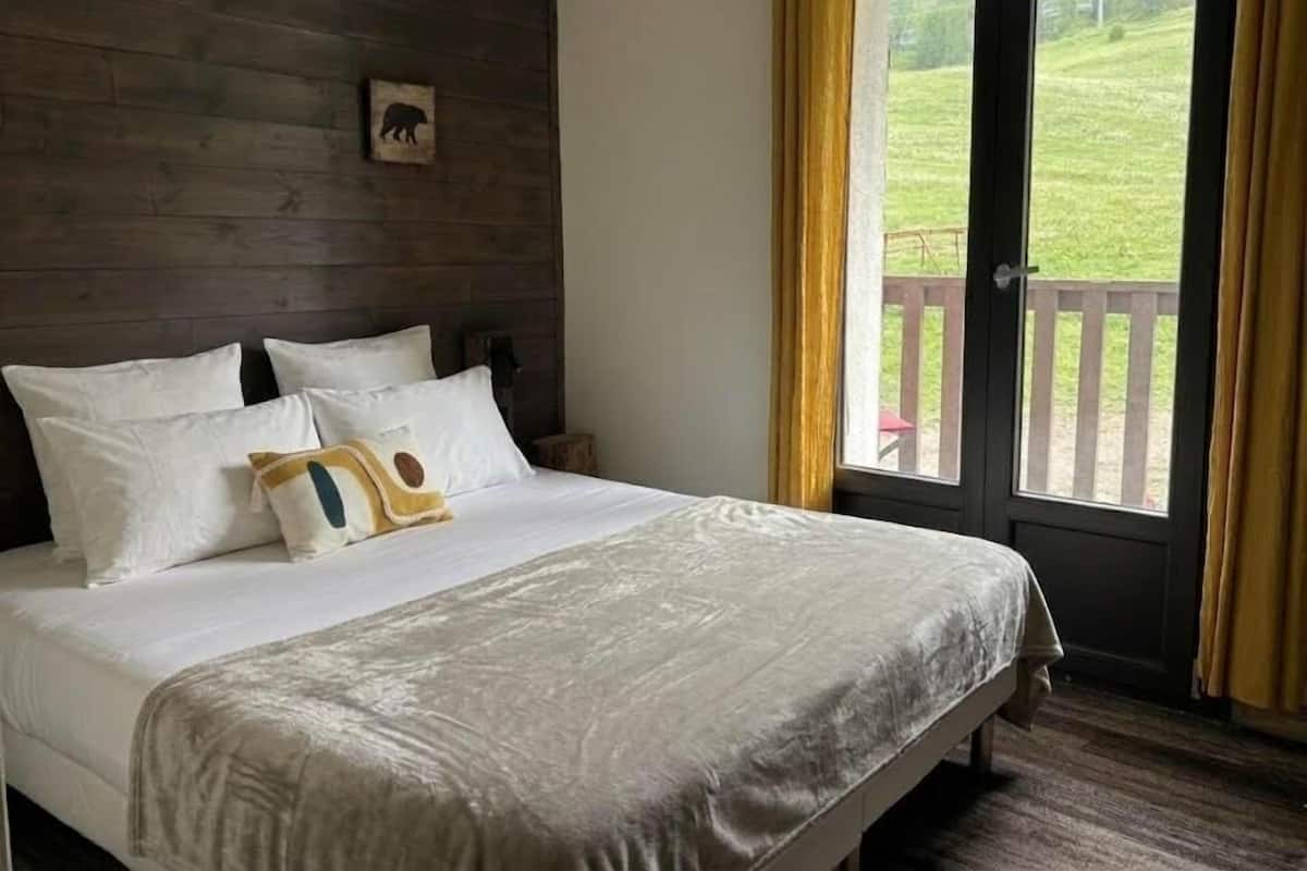 A bedroom with a bed, a wooden headboard, a picture of a bear, and a view of a grassy area through a door.