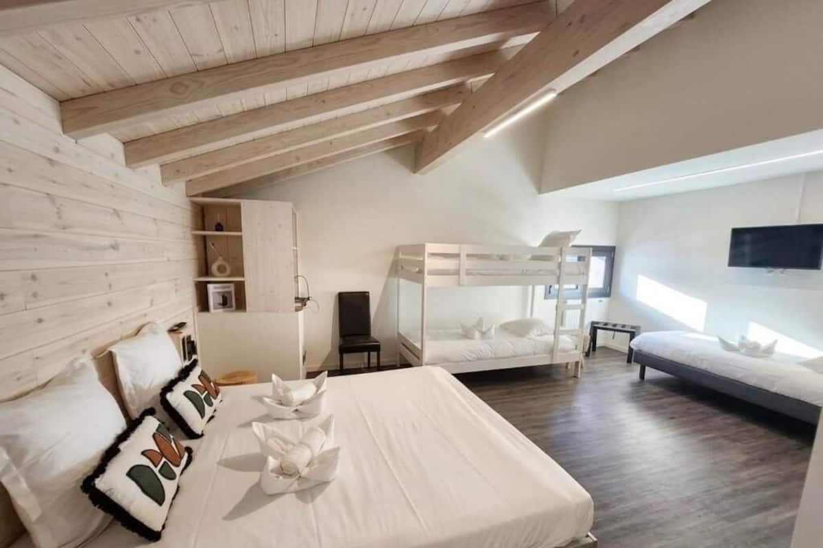 A bedroom with a bunk bed, a single bed, wooden beams, a TV, and a bedside table.
