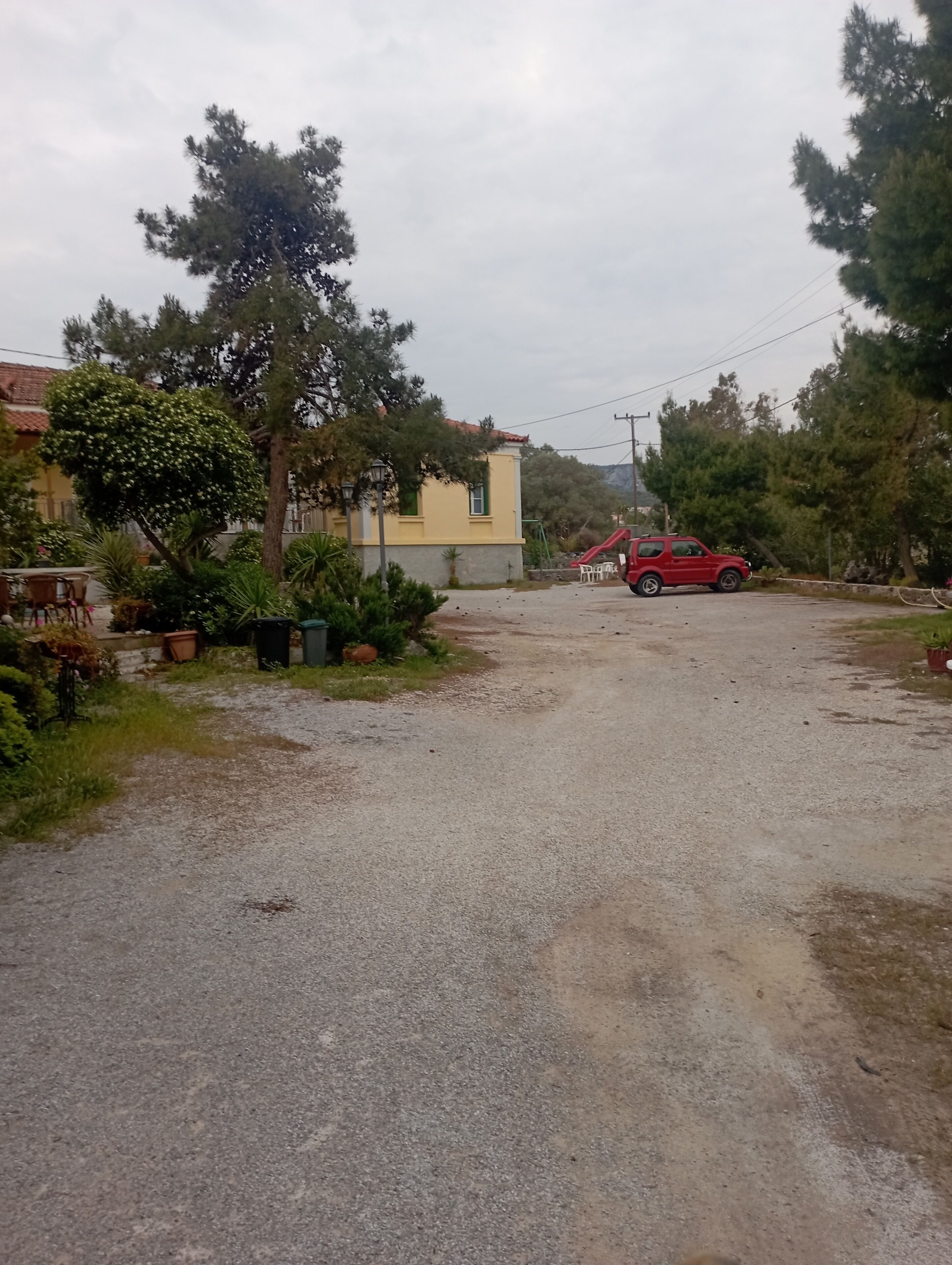 A residential area with a gravel driveway, a red car parked, and a yellow building with a red roof.