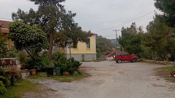 A residential area with a gravel driveway, a red car parked, and a yellow building with a red roof.