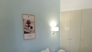 Un dormitorio con cama, mesita de noche, lámpara de pared, armario y un cuadro en la pared.
