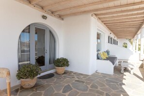 A covered outdoor area with a stone floor, a bench, and potted plants. - Blue Moon Mykonos Homes (Mykonos)
