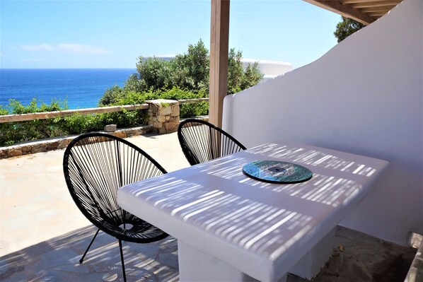 A white table with a blue plate, two black chairs, and a view of the sea.