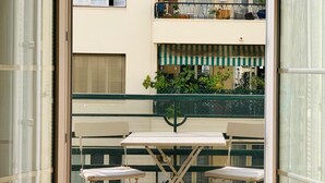 A balcony with a table and two chairs, a green safety net, and a view of a building with a green awning. - Chic & Spacious Getaway in Nice - 10 min to Beach (Nice)