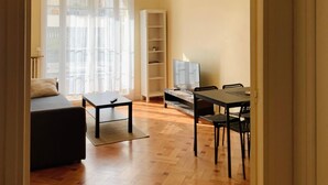 A modern living room with a sofa, a coffee table, a dining table with chairs, a TV, and a bookshelf. - Chic & Spacious Getaway in Nice - 10 min to Beach (Nice)