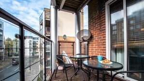 A balcony with a table and chairs, a brick wall, and a view of the street.