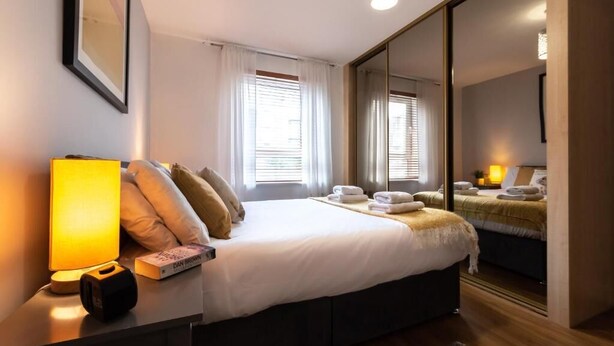 A modern hotel room with a large bed, bedside lamps, a bedside table with a book, and a mirror.