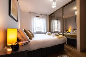 Ein modernes Hotelzimmer mit einem großen Bett, Nachttischlampen, einem Nachttisch mit einem Buch und einem Spiegel.