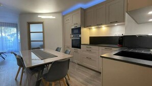 A modern kitchen with a dining area, featuring light-colored cabinets, a black countertop, and a built-in oven. - Superbe Appartement Cosy - Plage des Minimes (La Rochelle)