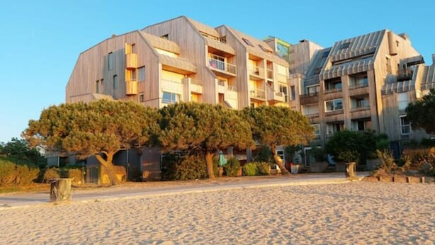 A modern building with multiple balconies and a sandy beach in the foreground. - Superbe Appartement Cosy - Plage des Minimes (La Rochelle)