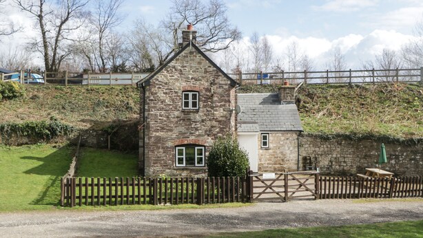 A stone house with a small attached garage, a wooden fence, and a gravel driveway. - Aqueduct Cottage (Pontypool)