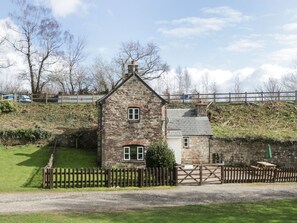 A stone house with a small attached garage, a wooden fence, and a gravel driveway. - Aqueduct Cottage (Pontypool)